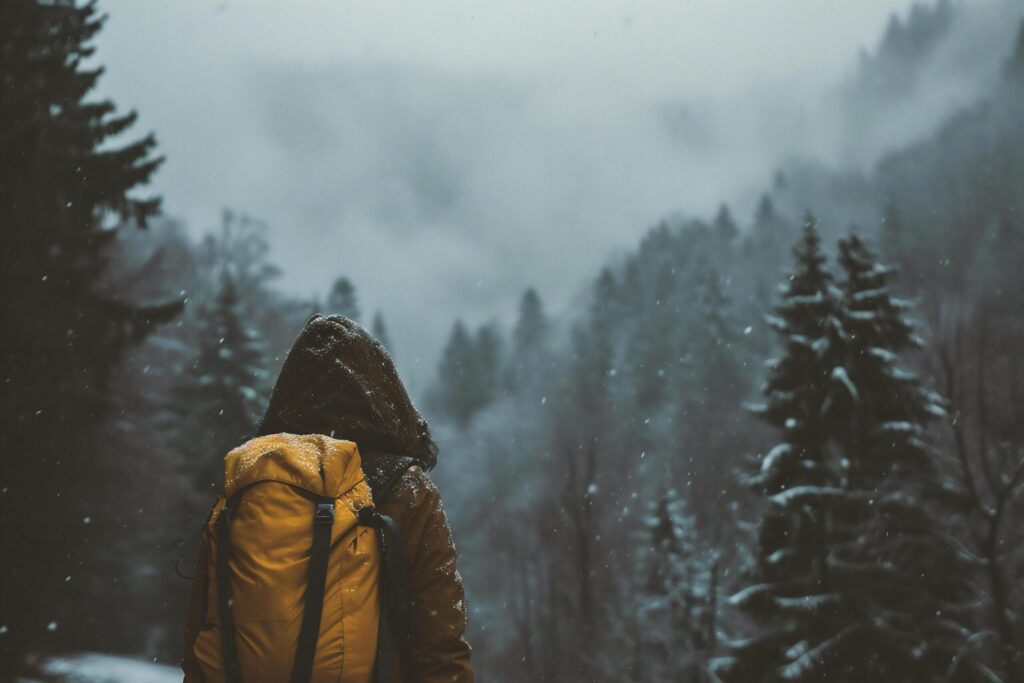 A woman in a yellow jacket with a backpack stands on the background of a snowy forest. Free Photo