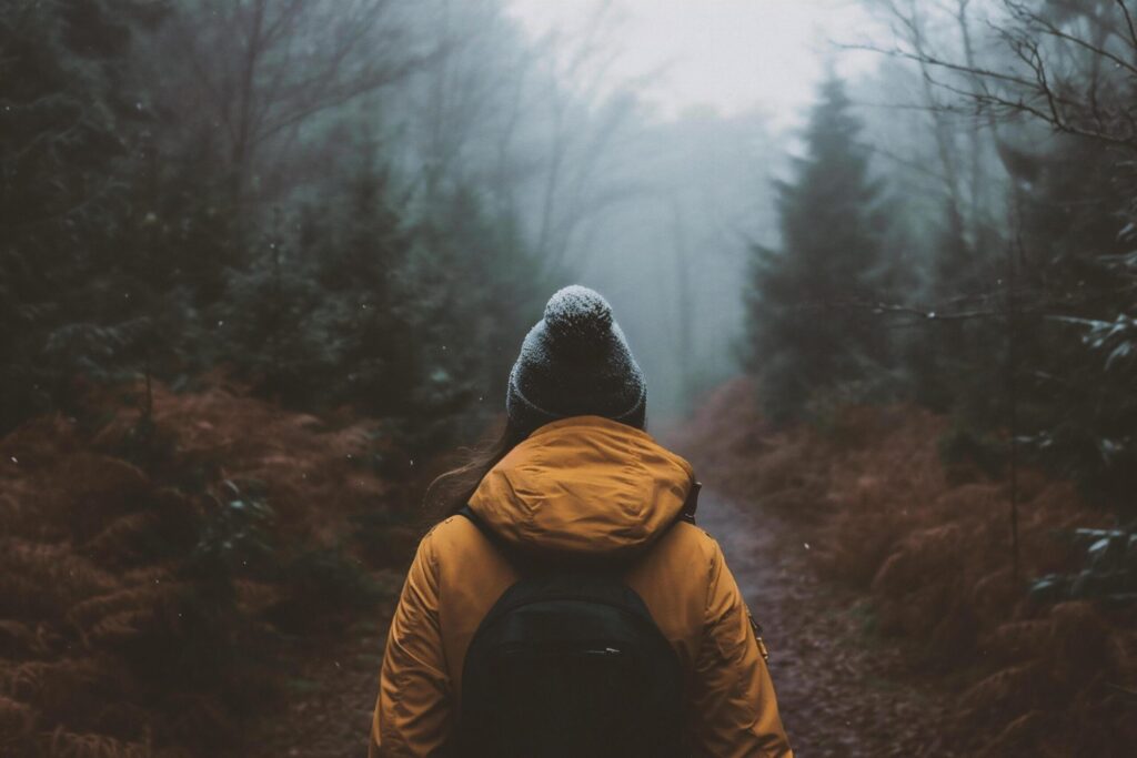 A young woman with a backpack on her back walks through the foggy forest. Free Photo