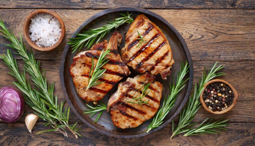 Grilled pork chops with rosemary sprigs on a wooden table, top view Free Photo