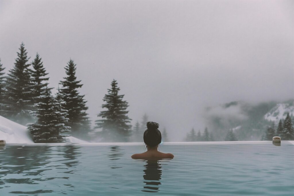 Woman relaxing in outdoor swimming pool with foggy mountains in the background Free Photo