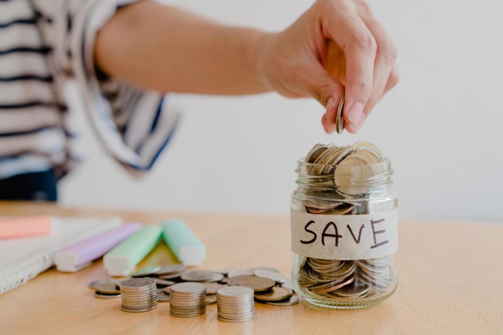 asian woman hand is putting a coin in a glass bottle on wooden table, Investment business, retirement, finance and saving money for future concept. Stock Free