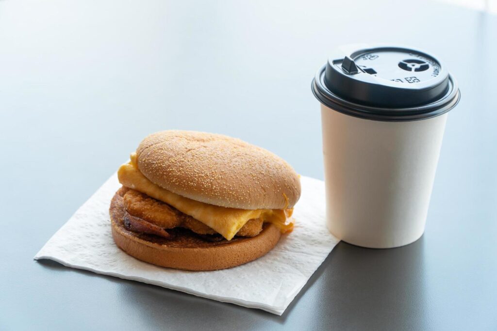 Bacon and Omelette Hamburger on the paper with White paper coffee mug on the table in fast food restaurant Stock Free