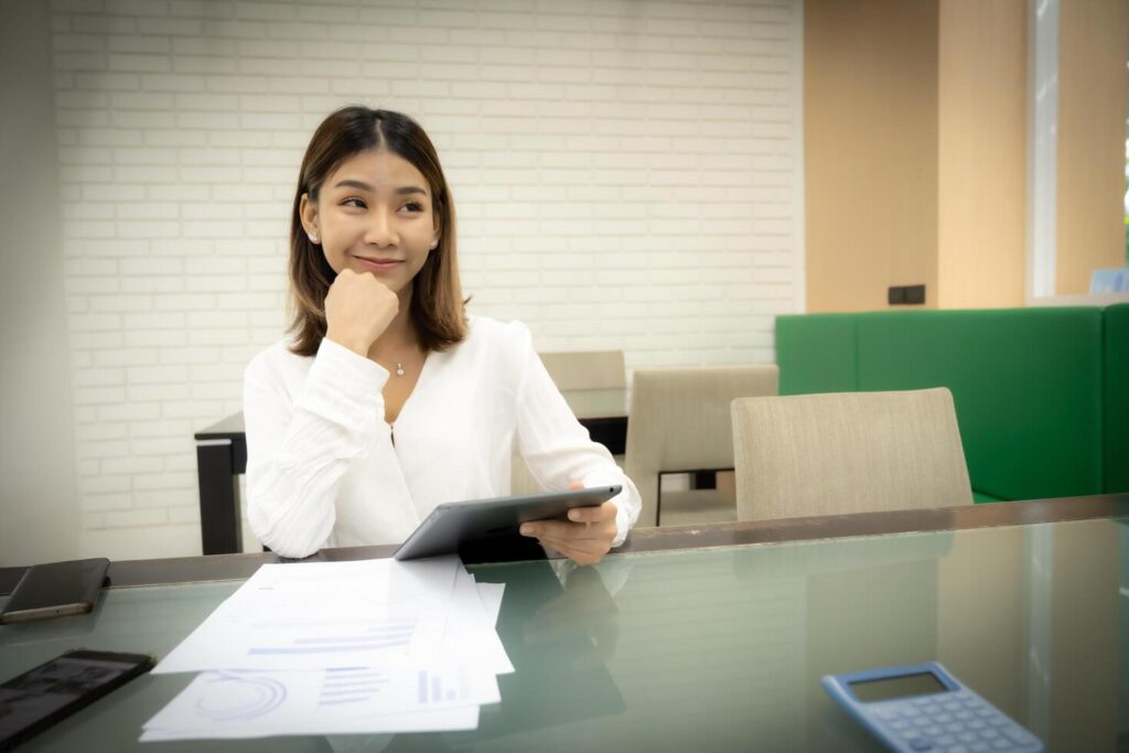 Beautiful asian business woman is sitting with a doubtful expression and holding tablet on her desk. Stock Free