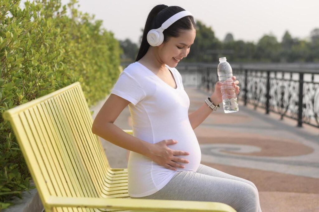 Beautiful pregnant woman drinking bottle of pure water in the park, Healthy and active pregnancy lifestyle concept. Stock Free