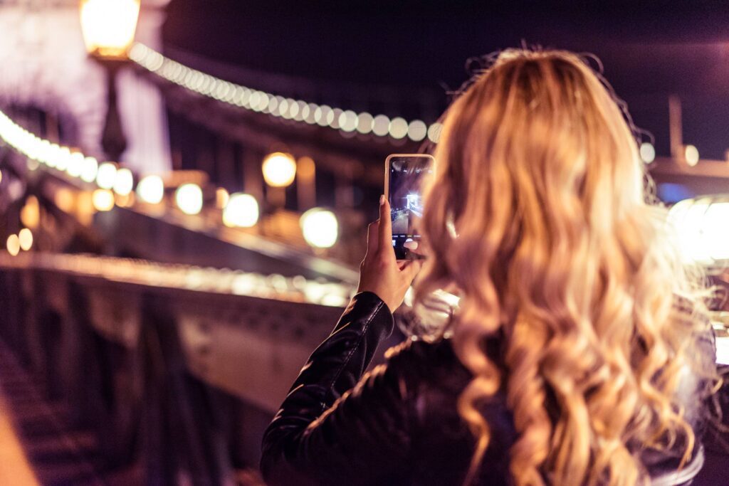 Blonde Woman Taking a Photo of an Old Bridge at Night Free Photo