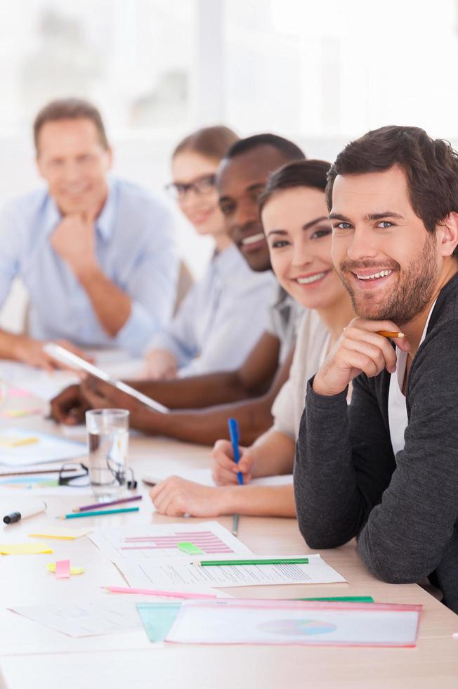 Business meeting. Group of business people in casual wear sitting in a row at the table and smiling at camera Stock Free