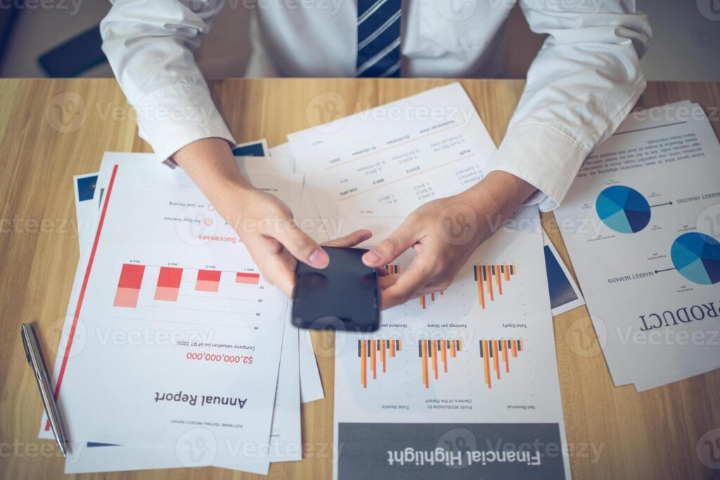 Business professional engaging with smartphone among various financial documents on a desk Pro Photo