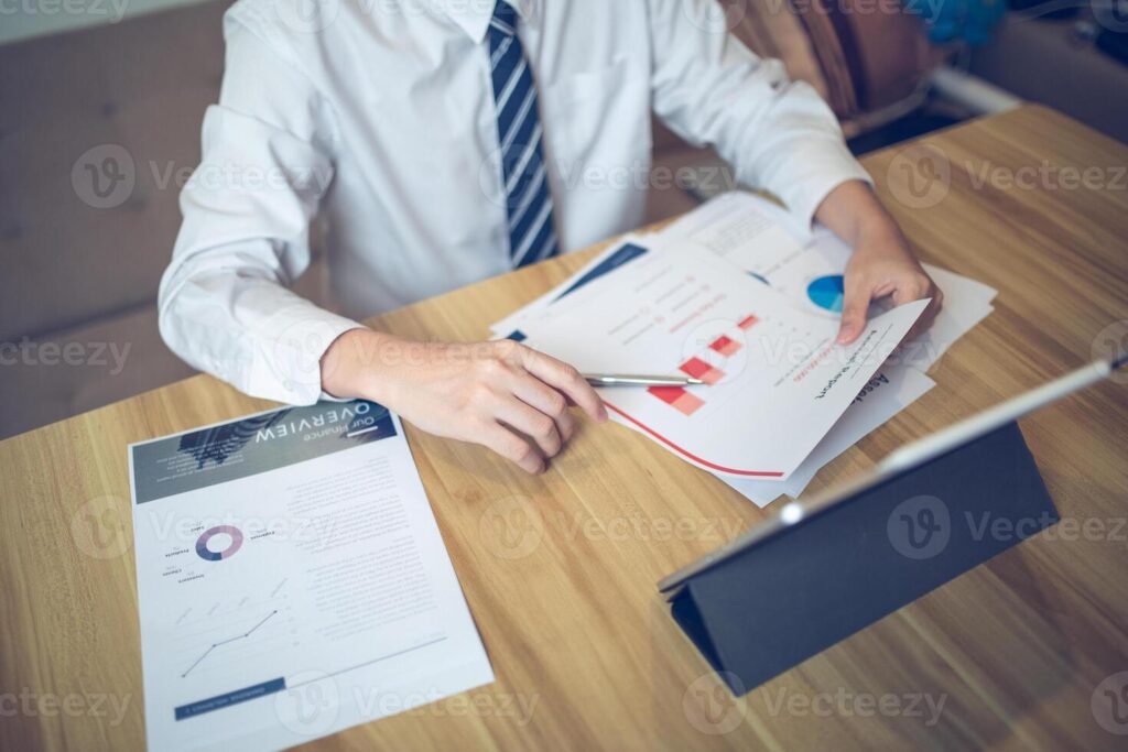 Businessman analyzing bar graph data with pen in hand, laptop and coffee on desk. Business concept Pro Photo