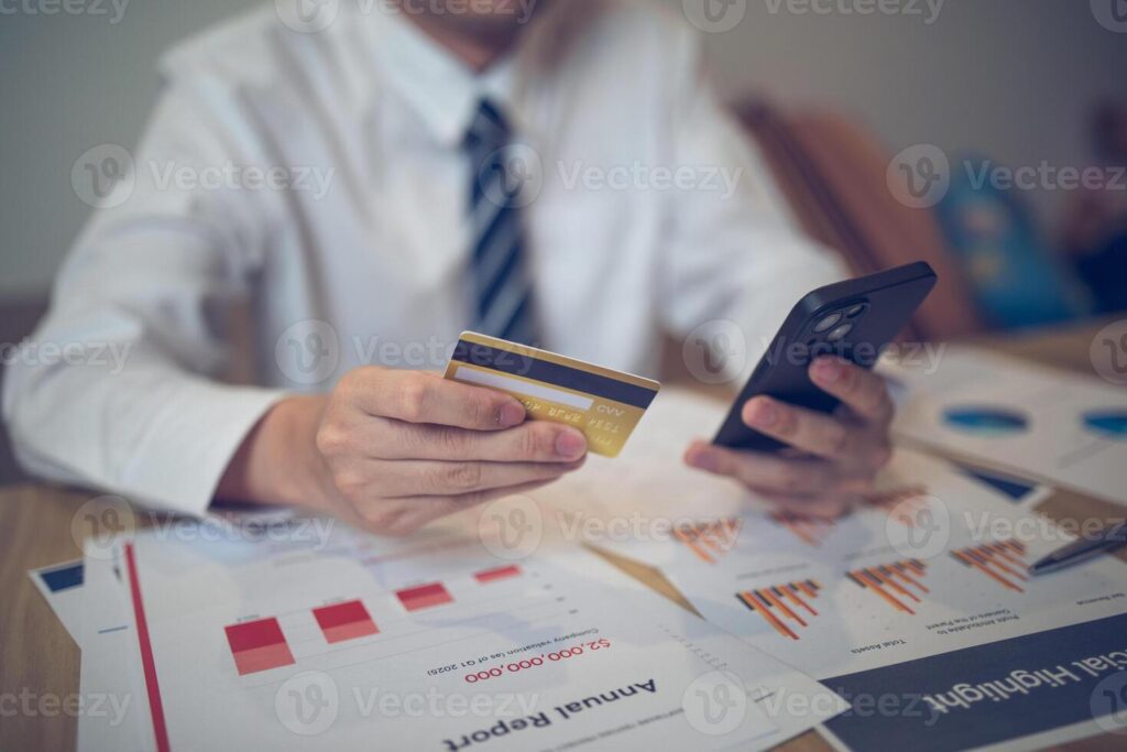 Businessperson holding a credit card and smartphone amid financial papers. E-commerce business concept Pro Photo