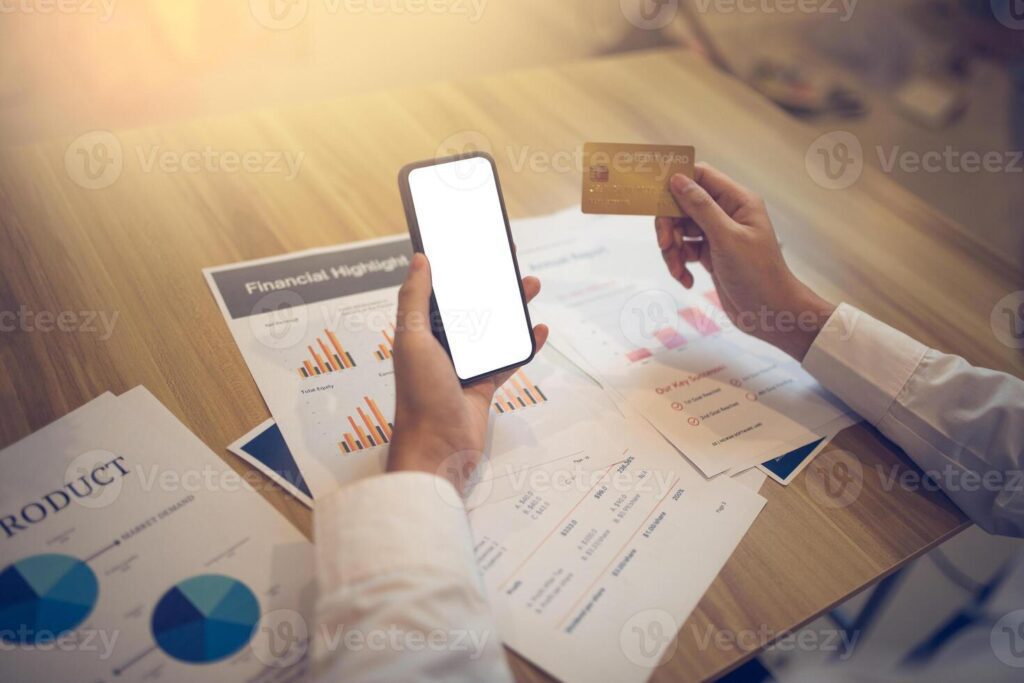 Businessperson holding a credit card and smartphone with mockup screen amid financial papers. E-commerce business concept Pro Photo