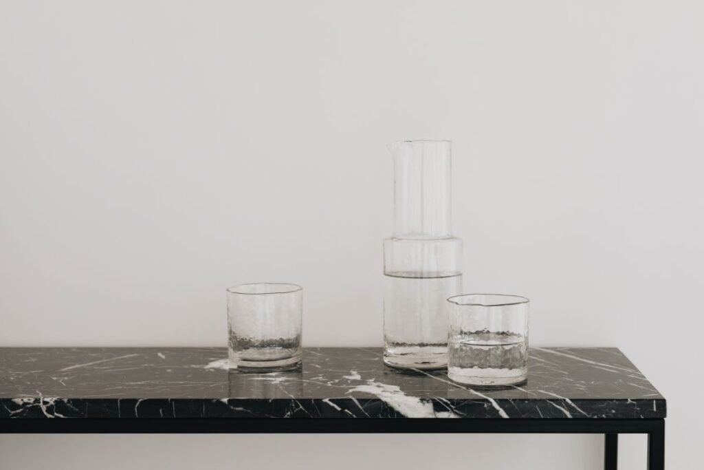 Water in a transparent glass carafe and glasses on a black marble console Stock Free