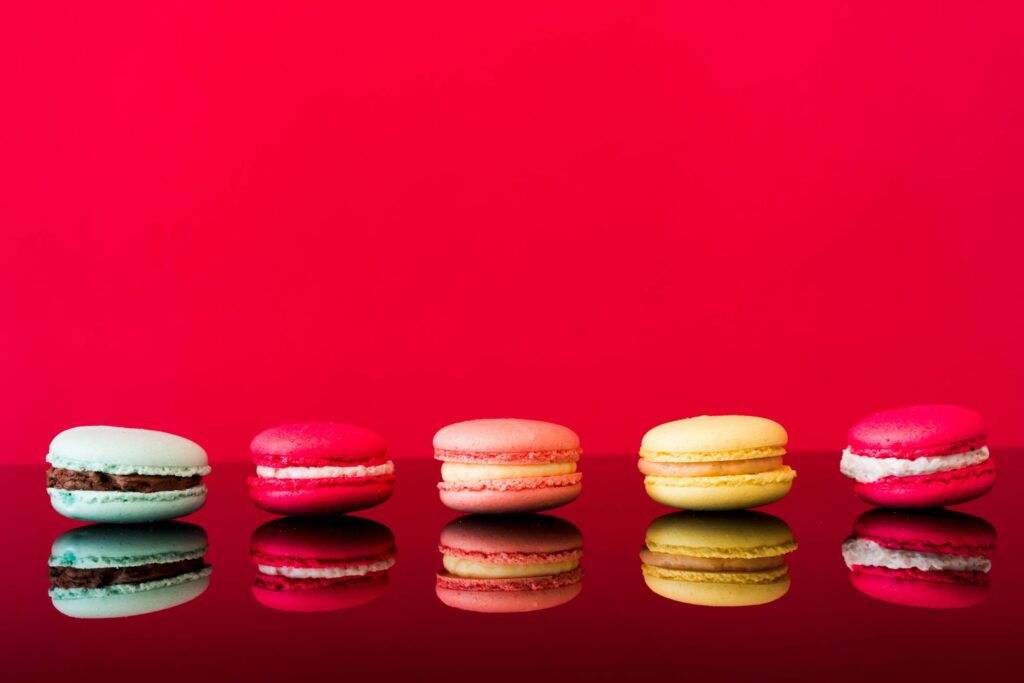 Colorful Yummy Macarons on Glossy Table and Red Background Free Photo