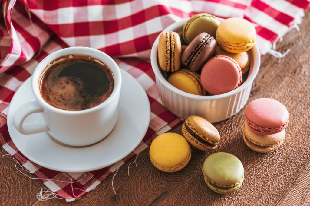 Colourful French Macarons with a Cup of Coffee on a Checked Cloth Free Photo