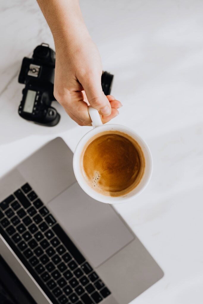 Creative Holding Cup of Coffee Over Laptop and Camera Free Photo