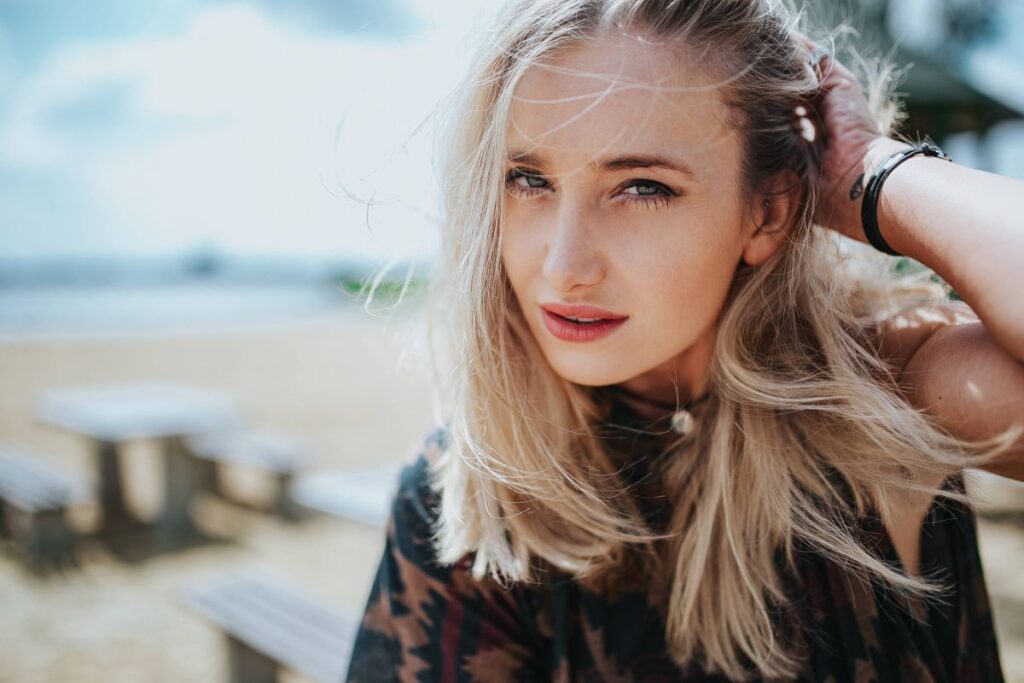 Beautiful blonde woman relaxing with a can of coke on a tree stump by the beach Stock Free