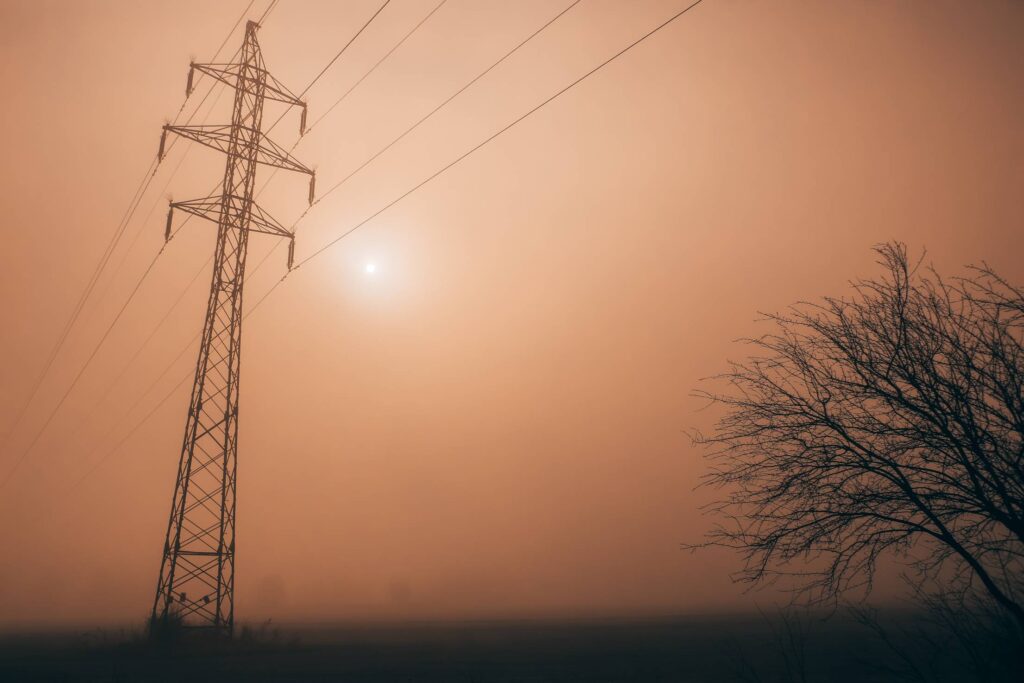 Electricity Power Lines Against Sun in Morning Fog Free Photo