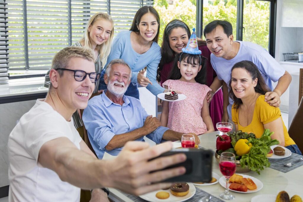 Father taking selfie photo using mobile phone for group photo in his daughter birthday party with whole big family and neighbor joining together in celebration meal Free Photo