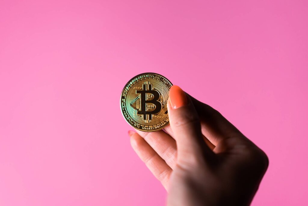 Female Hand Holding a Bitcoin on a Pink Background Free Photo