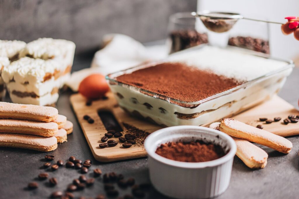 Female Hand Sprinkling Cocoa Powder on Tiramisu Free Photo