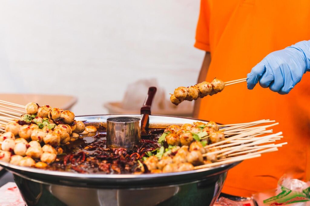 Food vendor hand holding pork meatballs in skewer with sweet chili sauce. Stock Free