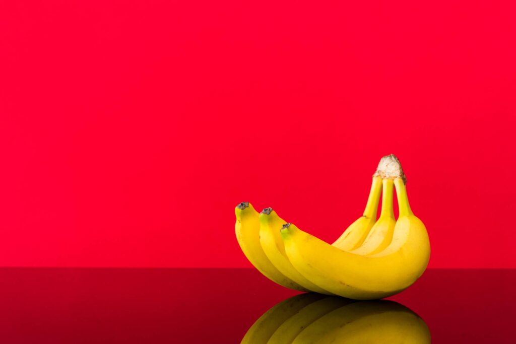 Fresh Bananas on Glossy Table and Red Background Free Photo