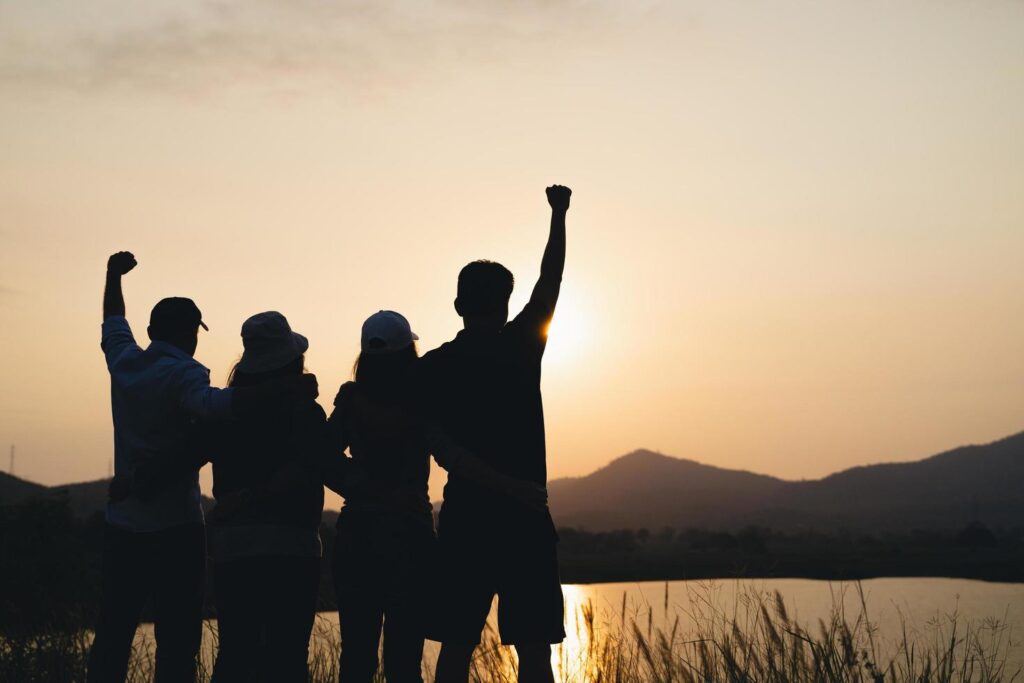 group of people with raised arms looking at sunrise on the mountain background. Happiness, success, friendship and community concepts. Stock Free