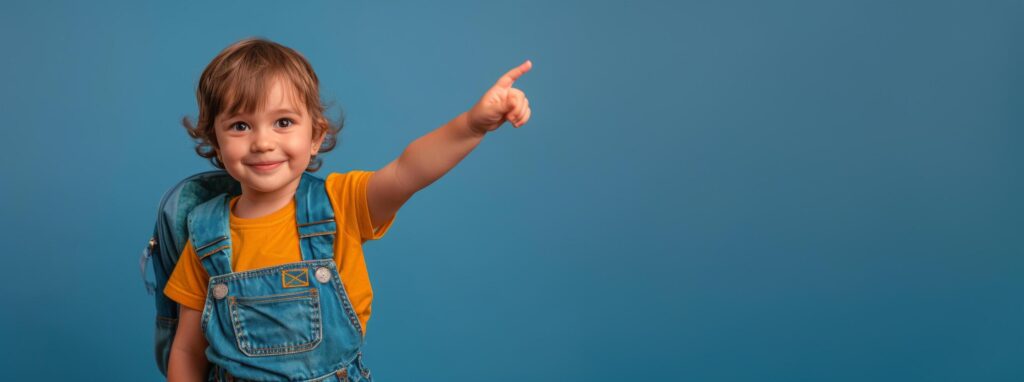 Happy Young Boy Pointing Towards Empty Space While Wearing Backpack on Blue Background Stock Free