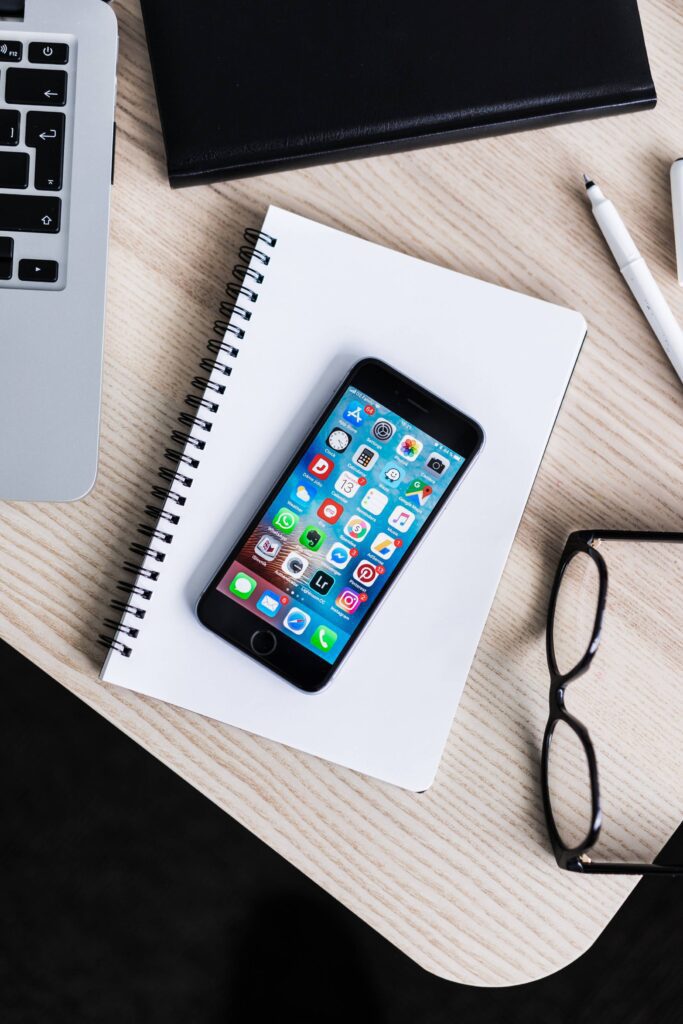 iPhone Lying on Notebook and Wooden Desk Mockup Free Photo