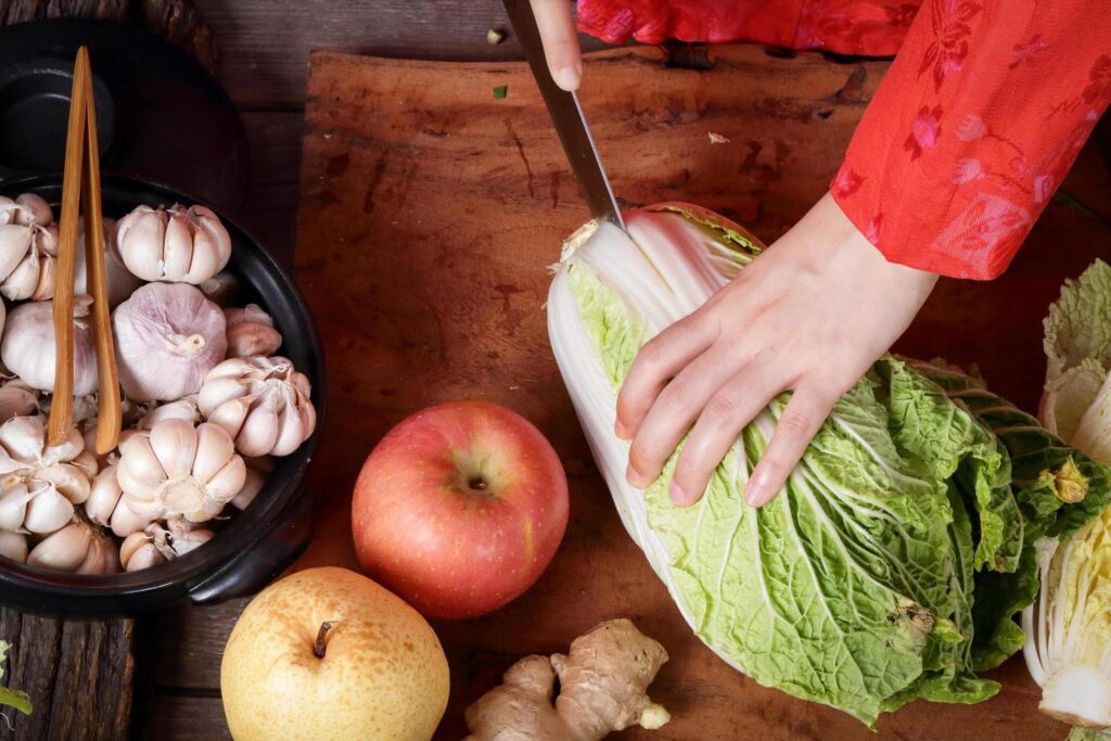 Korean women wear traditional red hanboks, make kimchi by slicing Chinese cabbage. The concept of cooking fermented, charming and fragrant, Asian food from folk wisdom Stock Free