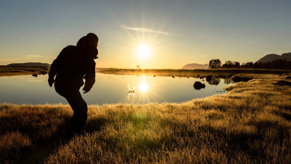 Man Throwing a Stone into a Calm Lake During Beautiful Sunrise Free Photo