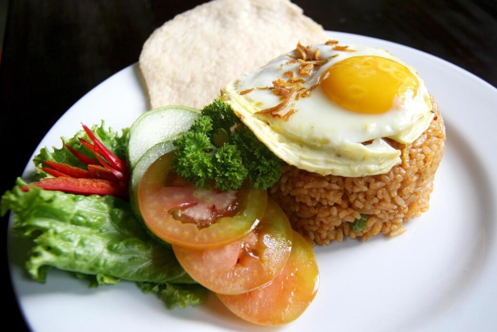 Nasi goreng fried rice with shrimps and egg garnished with fresh cucumber slices and prawn crackers on a white plate . Asian food. Stock Free