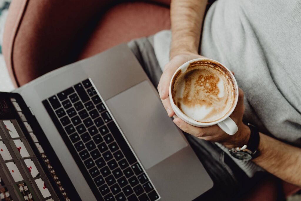 Nomad Freelancer Working on His Laptop and Holding a Cup of Cappuccino Free Photo