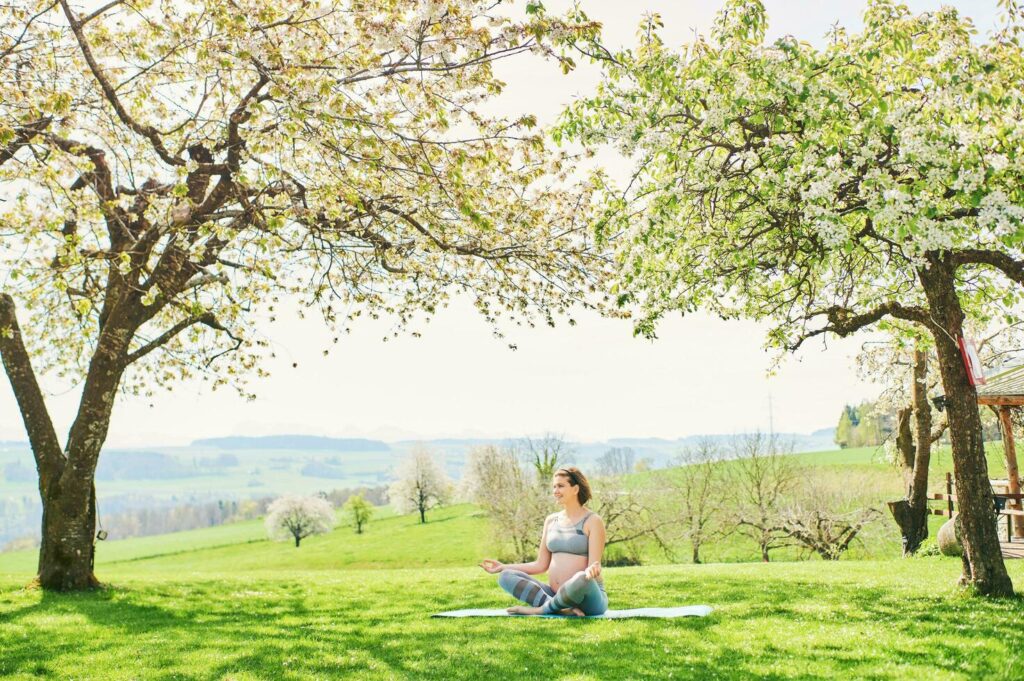 Outdoor portrait of happy young pregnant woman practicing youga in spring garden under blooming apple trees, healthy lifestyle Stock Free