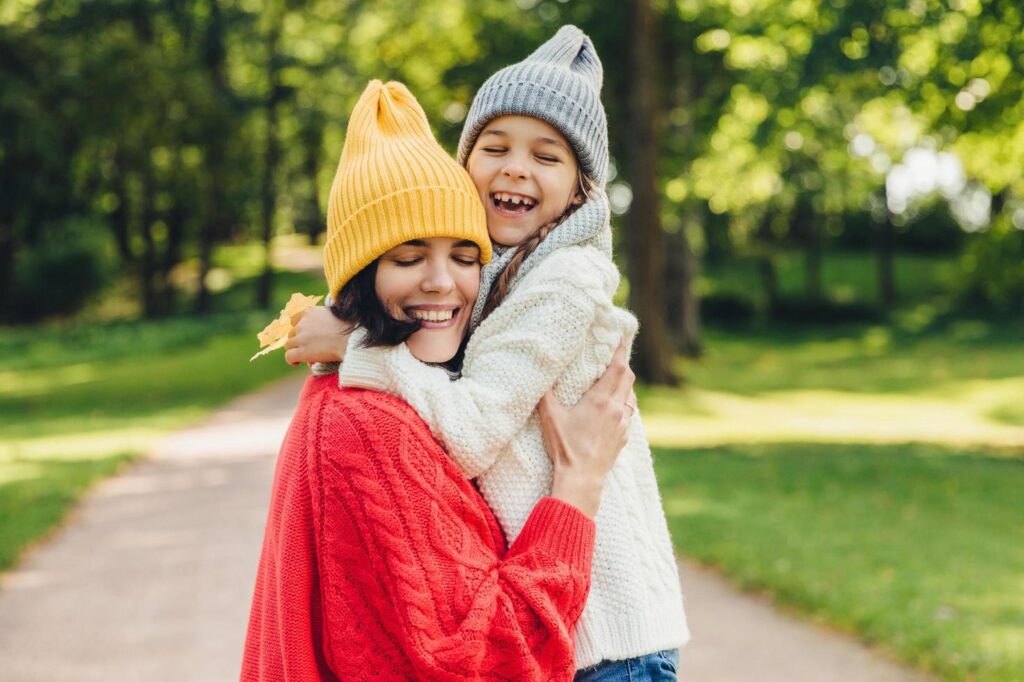 Parenthood, happiness and lifestyle concept. Beautiful female and her daughter have warm embrace, dressed in knitted clothes, have walk during autumn day, enjoy sunny weather, love each other Stock Free