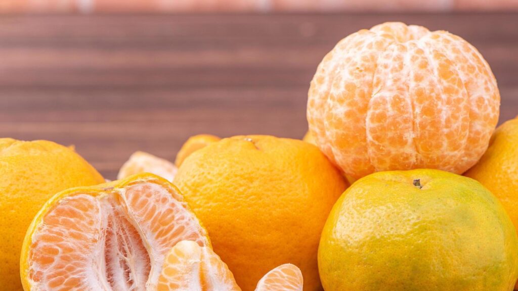 Peeled tangerines in a bamboo sieve basket on dark wooden table with red brick wall background, Chinese lunar new year fruit design concept, close up. Stock Free