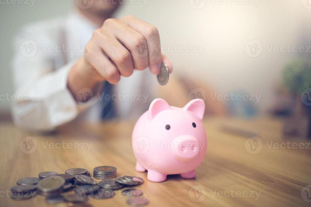 Person in a business shirt saving money in a piggy bank, with coins and financial reports on the table. Saving money business concept Pro Photo