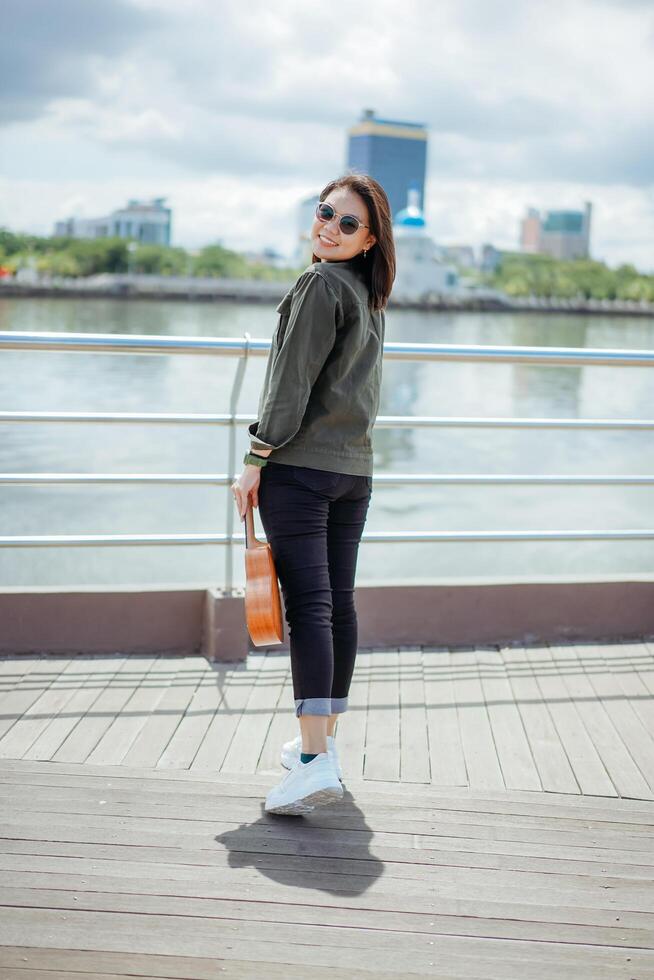 Playing Ukulele of Young Beautiful Asian Woman Wearing Jacket And Black Jeans Posing Outdoors Stock Free