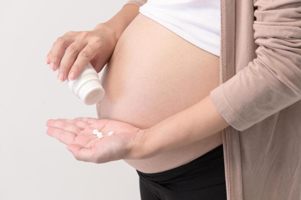 Portrait of Beautiful pregnant woman taking pill and vitamin over white background studio, health and maternity concept Stock Free