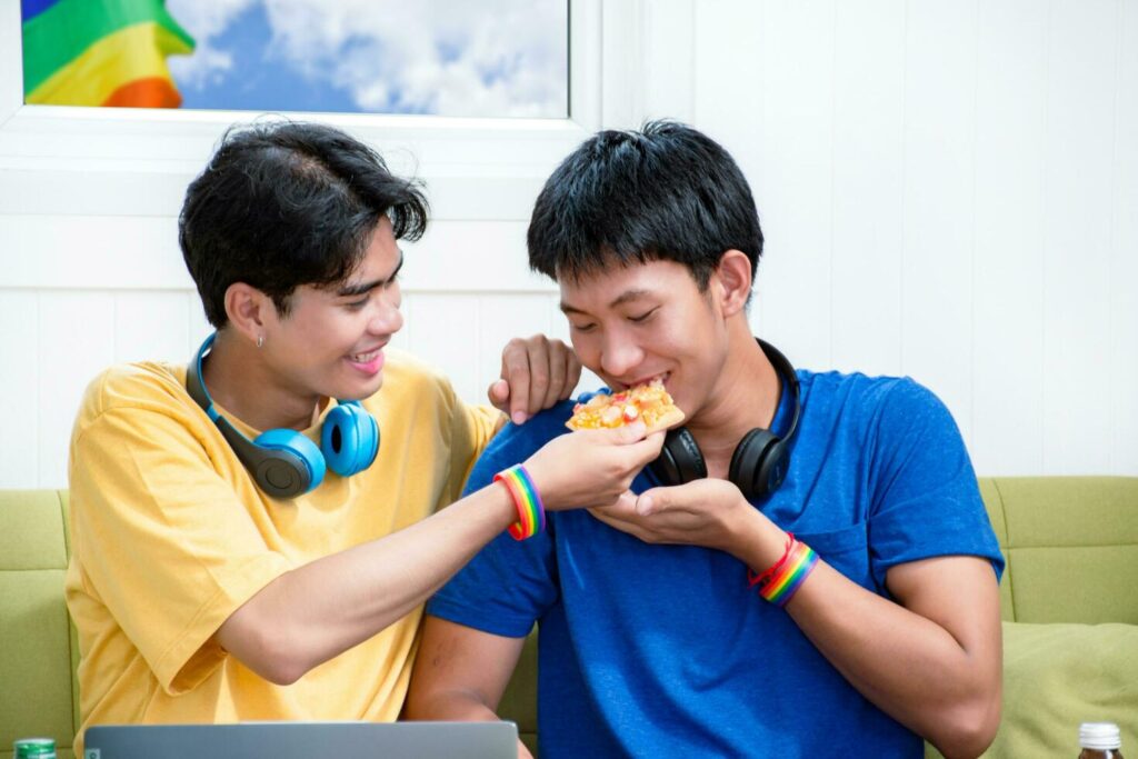 Portrait of two young asian gay couples sitting on sofa, spending their free time and watching tv at home together, concept for lifestyle of LGBT people around the world. Stock Free