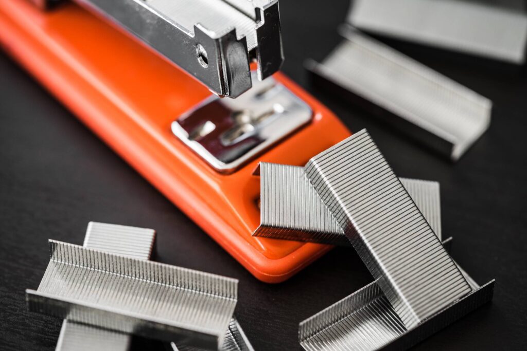 Red Office Stapler and Pile of Copper Office Staples Free Photo