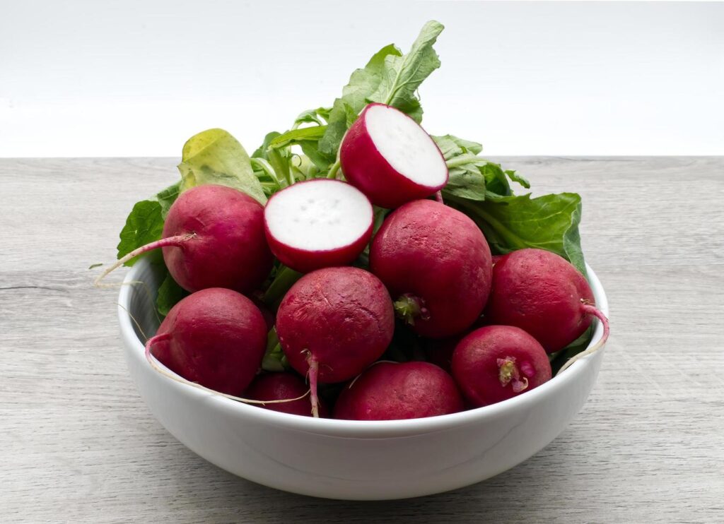 Red radishes in a bowl isolated on wooden background Stock Free