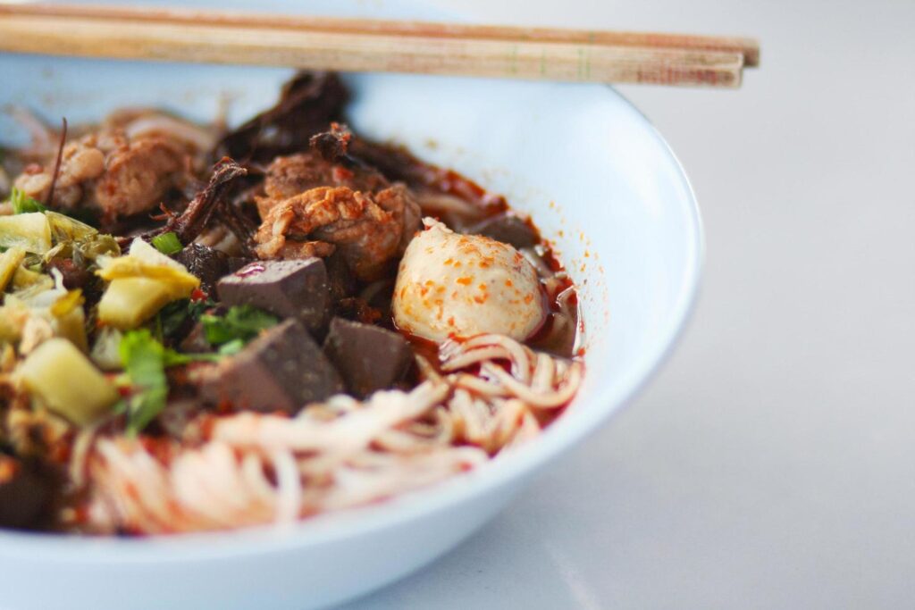 Rice noodles with spicy pork sauce in white bowl with chopsticks and spoon. Thai spicy food. Stock Free