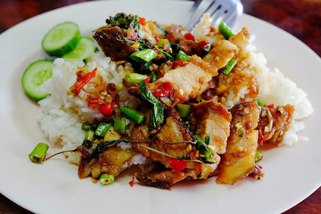 Rice topped with Stir Fried Spicy Crispy Pork and Thai basil on white plate.Tradition Thai food. Stock Free