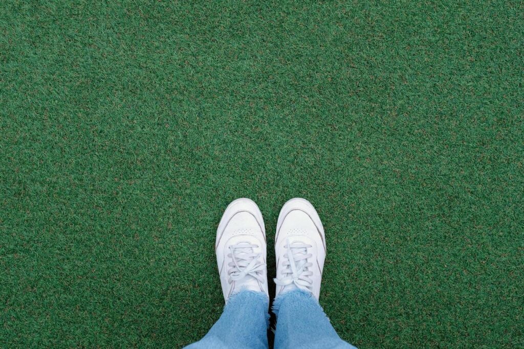 Selfie of feet in white sneakers shoes on green grass background with copy space, spring and summer with fashion lifestyle concept Stock Free