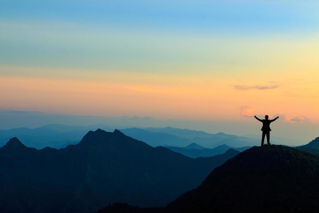 silhouette of businessman on mountain top over sunset sky background, business, success, leadership and achievement concept Stock Free