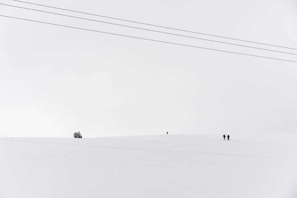 Snow Covered Hill with Tiny Cross-Country Skiers Free Photo