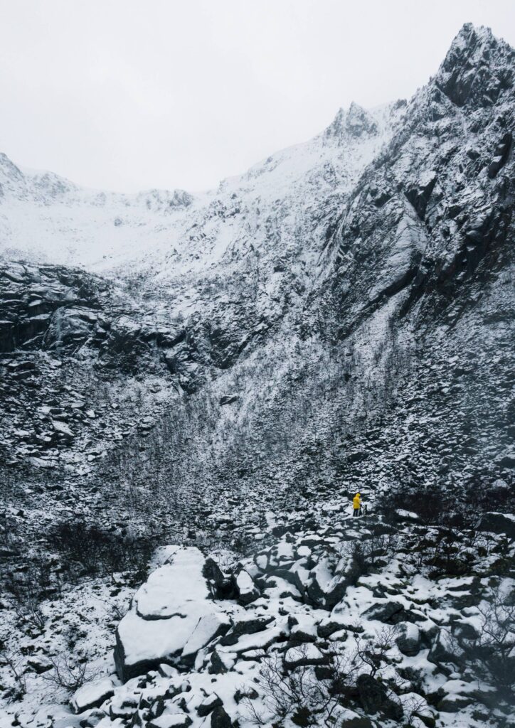 Tiny Person in Yellow Jacket Standing between Rocks Covered by Snow Free Photo