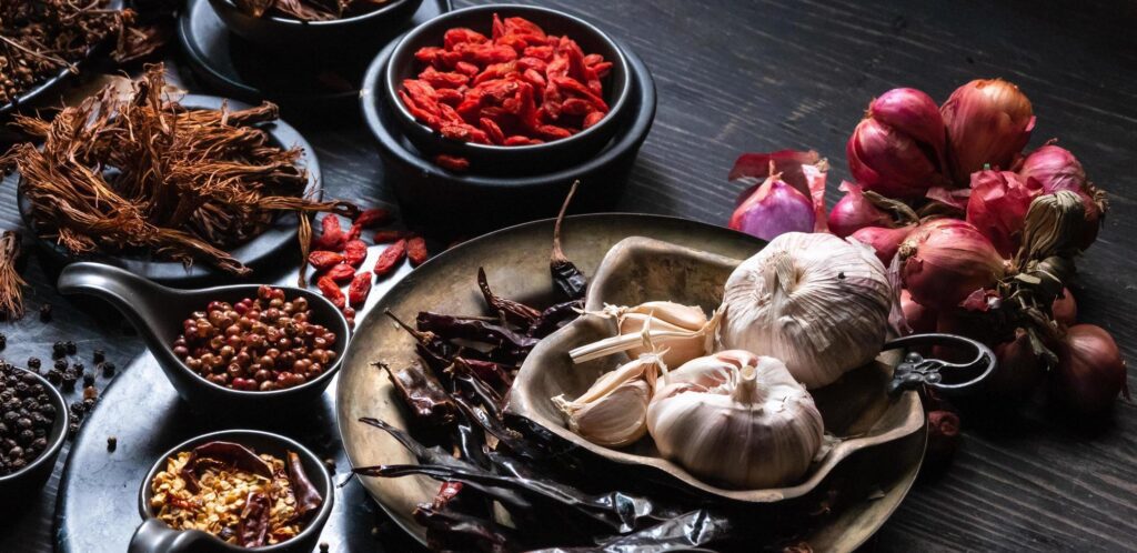 Top view photo Lots of garlic, onions, peppers, chili and dried herbs, were placed on plates and cups on a black wooden drak background. was divided To prepare to cook food india healthy food Stock Free