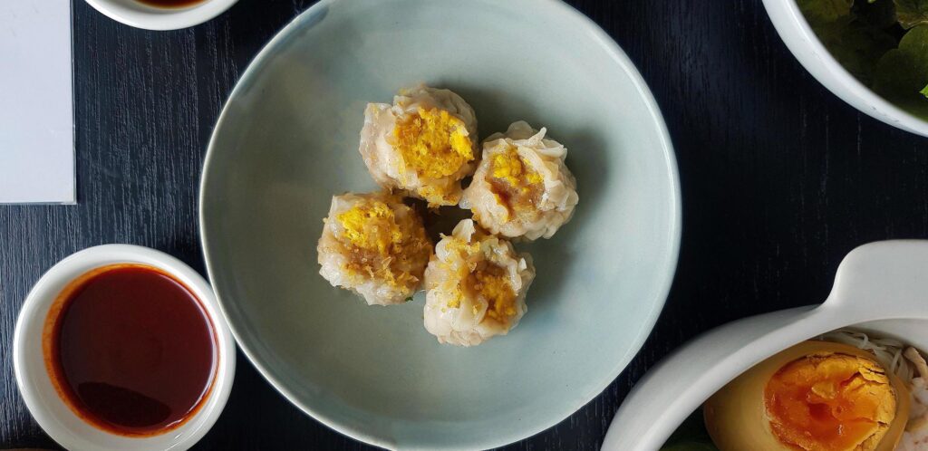 Top view of four steamed dumplings on green dish with sliced boiled egg and sweet sauce. Chinese food with fried garlic topping. Flat lay of Asian snack and Famous food in Asia Stock Free