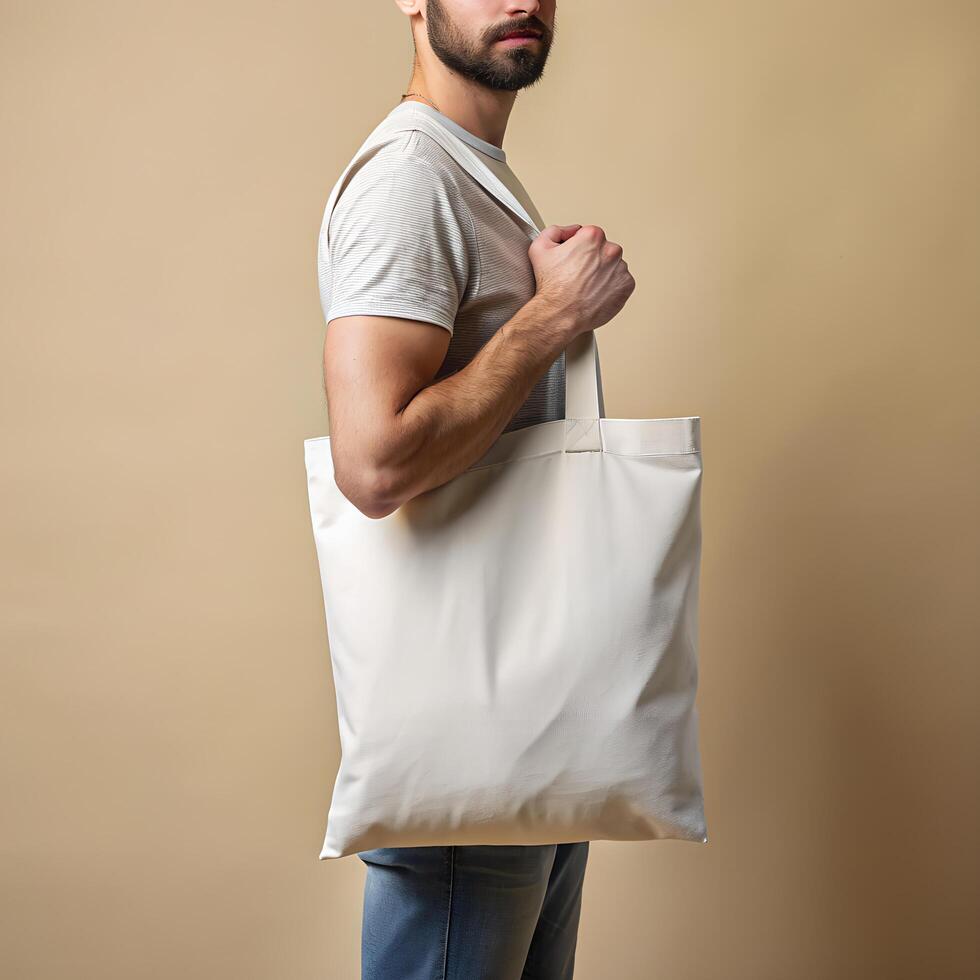 Tote bag mockup. Man carrying reusable white cotton linen eco organic fabric canvas blank totebag on beige background. Stock Free